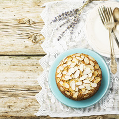 Simple homemade pecan pie decorated with petals of almond  a wooden background Serving Easter used blue and yellow colors, quail eggs, lavender flowers, vintage linen tablecloth handmade.