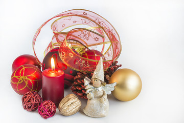 Christmas compositon with burning candle, angel figurine, red and golden christmas balls, red ribbonn on white background