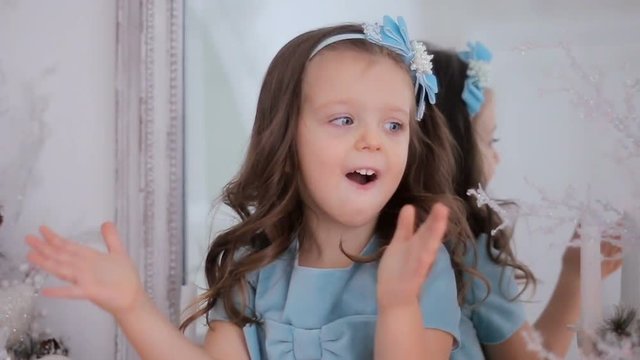 little girl in a blue dress sits at a mirror and claps his hands