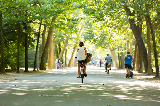 Women bikes through a sunny Vondelpark.