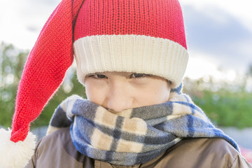 Closeup of boy wearing santa hat, nuzzled into a scarf walking o
