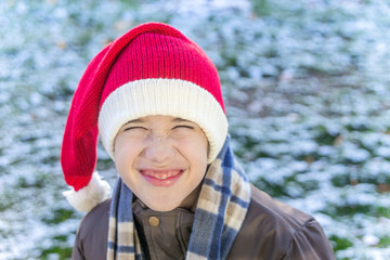 Fototapeta na wymiar Boy outside wearing a knitted santa cap, laughing and scrunching