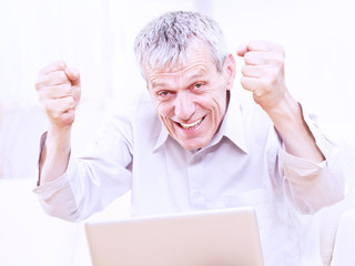 Excited senior business man working on a laptop indoor