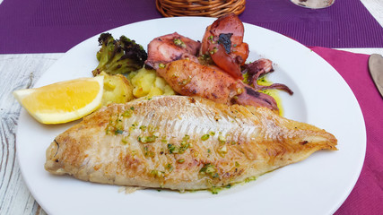 Grilled fish and squid with vegetables in the plate on the table / yummy fish fillet with mixed vegetables.