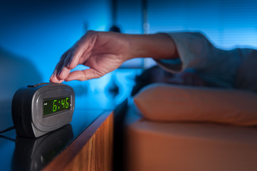 Woman pressing snooze button on early morning digital alarm clock