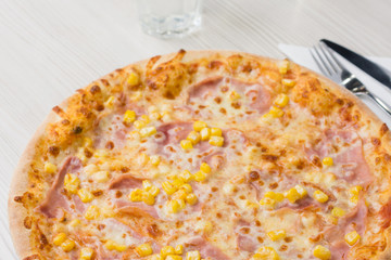 Detail of delicious pizza with ham and corn on the table