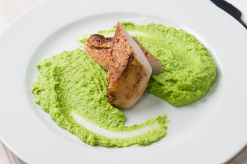 Detail of grilled chicken steak with mashed green peas up on a plate