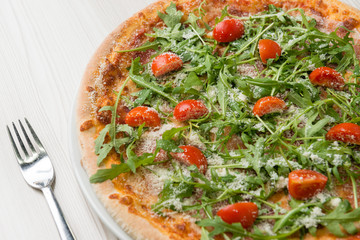 Delicious pizza with prosciutto, tomato, rucola and cheese on the table