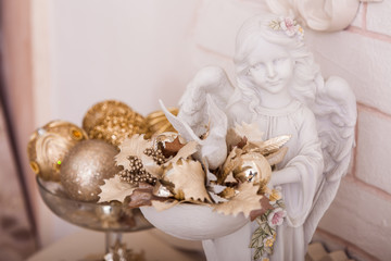 Angel statuette holding a bowl with golden Christmas ornaments