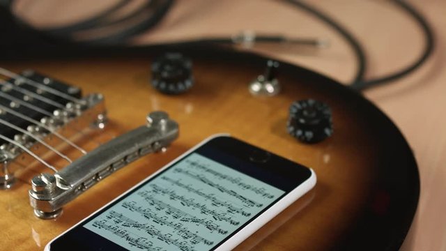 Close up of male hand put smartphone with notes on vintage electric guitar, online music school concept