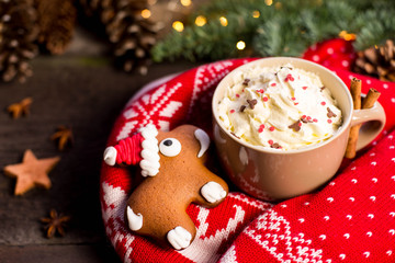 Cup of cocoa with cream and gingerbread against pine branches and traditional knitted sweater. Xmas concept.