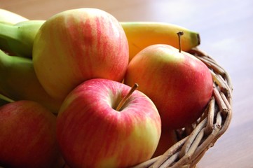 detail of wicker basket full of red apples and bananas on wooden table
