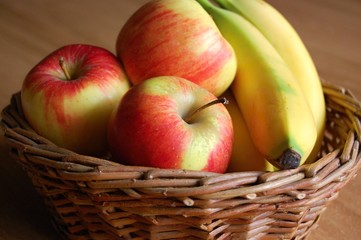 detail of wicker basket full of red apples and bananas on wooden table