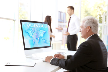 Man working with computer at office. Word LOGISTICS and world map on monitor. Business concept.