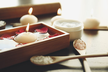Spa set with nutrient cream, sea salt in spoons and candles on wooden background