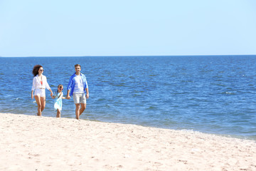 Fototapeta na wymiar Family concept. Parents with daughter holding hands and walking on sea shore