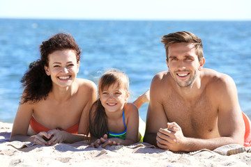 Portrait of cheerful family lying on sand on sea background
