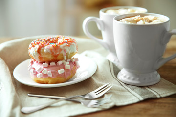 Plate with delicious doughnuts and cups of coffee on the table