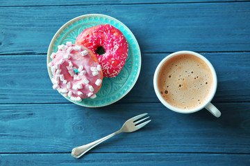 Plate with delicious doughnuts and cup of coffee on blue wooden table