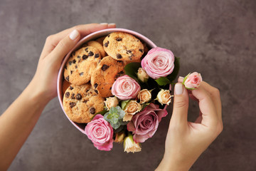 Female florist preparing box with beautiful flowers and cookies, closeup