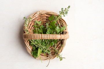 High angle view of thyme and parsley in small wicker basket on limestone background (selective focus)