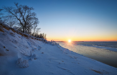 Winter landscape with frozen lake and sunset sky. Composition of