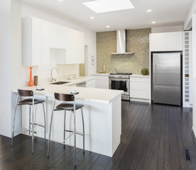 Modern kitchen interior in white with bar stools and wooden floor.