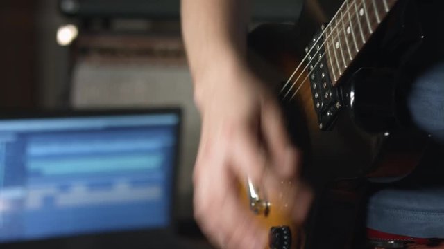 Guitarist playing rhythm on electric guitar and recording session with multitrack recording software on laptop