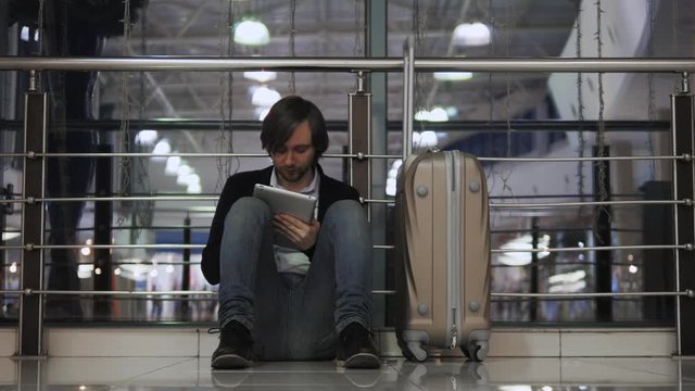 problem with transportation, delay of flight, depressed man with his luggage and tablet, headache and red eyes
