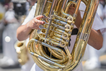 Tuba player in a military or marching band playing during a parade or festival on a sunny day. Wearing a white uniform with the brass instrument shining gold in the sun.