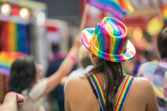Young brunette woman in a crowd celebrating Pride Parade. Wearing colorful rainbow accessories. Soap bubbles floating around her. Supporting marriage equality and LGBT rights.