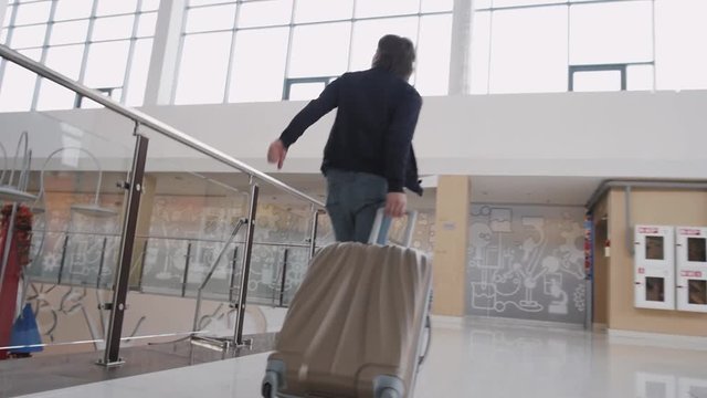 Unrecognizable man with suitcase hurrying. Businessman runing with laggage in airport terminal or train station.