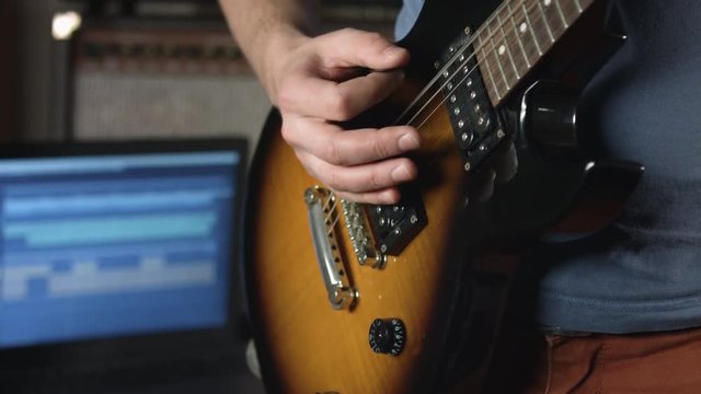 Close up of man playing rhythm on electric guitar and record result with multitrack music software on laptop