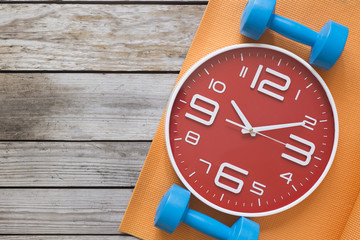 Time for exercising clock and dumbbell with yoga mat background