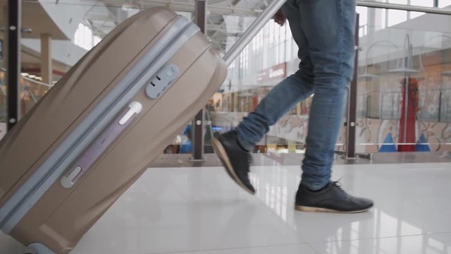 Young man pulling suitcase in modern airport terminal. Travelling guy wearing smart casual style clothes walking away with his luggage while waiting for transport. Rear view. Close-up