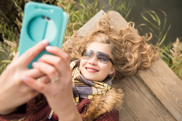 Smiling woman in sunglasses lying on the pier making a selfie