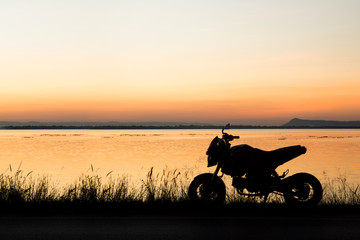 Obraz na płótnie Canvas Motorcycle in silhouette at sunset at lake.