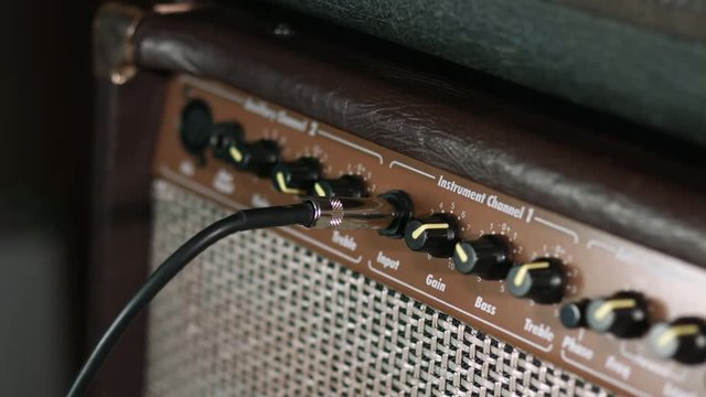 Close Up Of Male Hand Plugging In Guitar Cable In Cabinet Amplifier Jack