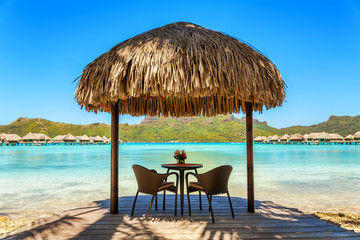 Two chairs and coffee table under a thatched parasol on a sand b