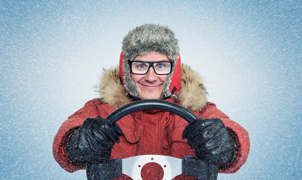Happy Man in winter clothes with a steering wheel, snow blizzard. Concept car driver.