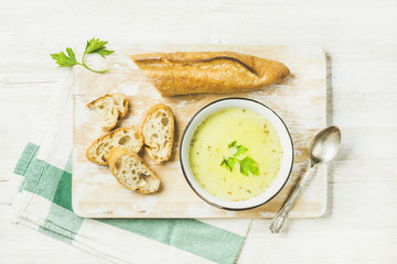 Green vegetable soup with parsley and baguette on white shabby wooden board over white painted...