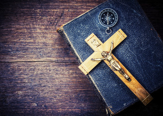 The crucifix of jesus and the compass on holy bible with on wooden background