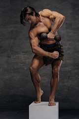 Muscular male posing on podium and holds dumbbell.