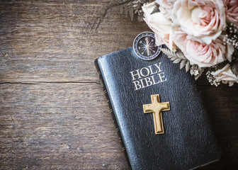 the wooden cross with compass and holy bible and roses flowers on wooden background, vintage tone...