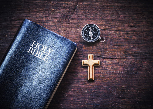the holy bible with small wooden cross and compass on wooden background