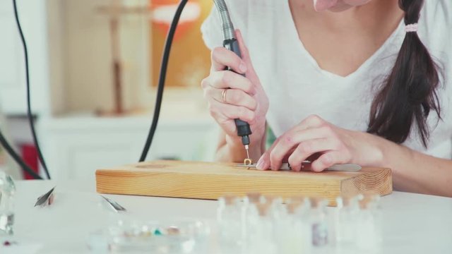 Young brunette makes handmade jewelry. Master class for creating jewelry. The pretty woman making jewelry and jewelry uses a drill. Master chooses jewelry accessories for decoration. lamp work