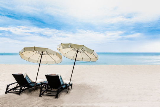 Beach chairs with sun shade on the white sand beach with cloudy blue sky and sun