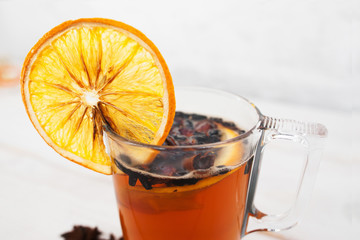 Hot winter drink with spices and orange, close-up. Glass of tea with citrus on white background. Refreshment, drink, winter beverage concept