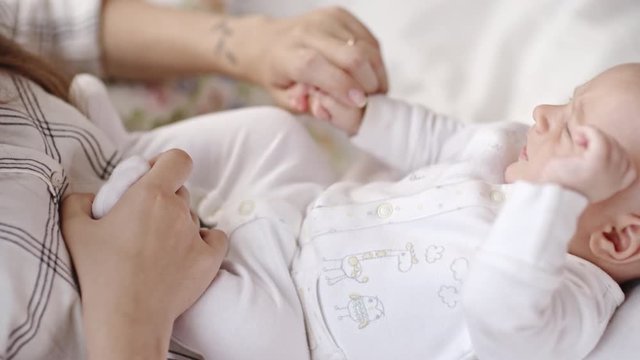 Young mother rocking fussy infant baby boy lying on her laps