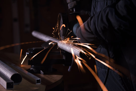 Worker Sawing Metal Pipe With A Electric Rotary Angle Grinder On An Working Table And Generating Sparks, Cutting